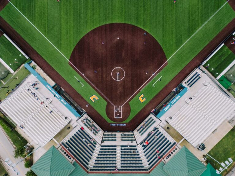 Aerial drone view straight down onto a college baseball/softball diamond and stadium seating, symmetric infield, foul lines, and dugouts at Frost Stadium.