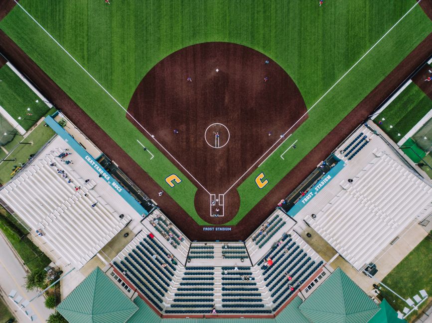 Aerial drone view straight down onto a college baseball/softball diamond and stadium seating, symmetric infield, foul lines, and dugouts at Frost Stadium.