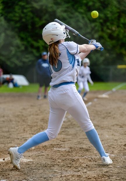 Youth softball player making contact mid-swing during a game