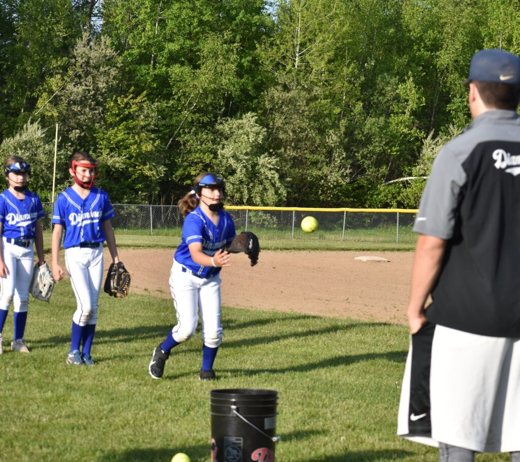 Diamond Softball Club coach watches a player mid-throw during a fielding drill as teammates wait their turn